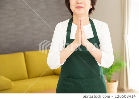 A middle-aged woman housewife wearing an apron making a wish in the living room at home 120508414