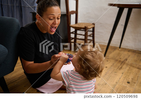 A delighted mother shares a playful moment with her young child on a wooden floor, capturing a sense of warmth and connection. Casual home setting evokes comfort and family bonding. 120509698