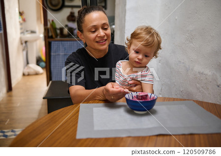Grandmother feeding grandson at kitchen table with care Grandmother feeding grandson at kitchen table with care 120509786