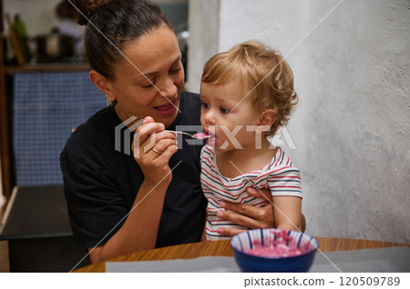 Mother feeding her toddler healthy homemade berry yogurt meal 120509789