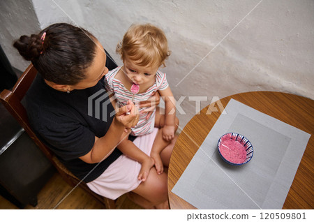 Mother feeding her toddler breakfast in the kitchen Mother feeding her toddler breakfast in the kitchen 120509801