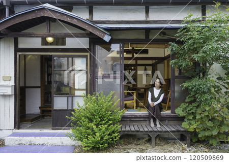 A middle-aged woman sitting on the veranda of an old house 120509869