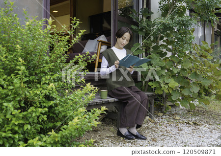 一位中年婦女坐在民宅的門廊上看書 120509871