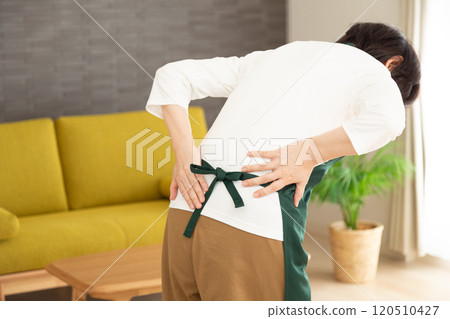A middle-aged woman wearing an apron suffering from back pain 120510427
