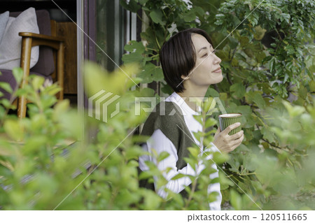 一位中年婦女坐在民宅的門廊上喝著飲料 一位中年婦女坐在民宅的門廊上喝著飲料 120511665