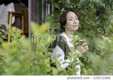 一位中年婦女坐在民宅的門廊上喝著飲料 一位中年婦女坐在民宅的門廊上喝著飲料 120511666