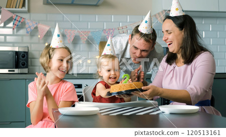 Cute baby girl, surrounded by her family, blows out the candle on her birthday cake while everyone claps and cheers, creating a special moment at home 120513161