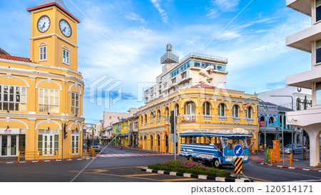The iconic yellow clock tower and historic Chartered Bank building in Phuket Old Town, showcasing Sino-Portuguese architecture, frame a bustling intersection with a blue local bus passing by 120514171