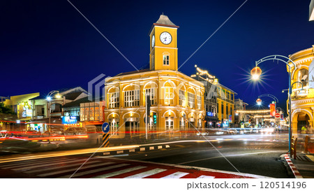 Night view of the Phuket Old Town Clock Tower illuminated with vibrant yellow lights, featuring bustling traffic light trails and cultural street decorations. Night view of the Phuket Old Town Clock Tower illuminated with vibrant yellow lights, featuring bustling traffic light trails and cultural street decorations. 120514196