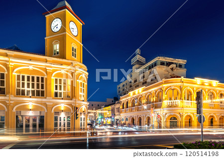 Night view of the Phuket Old Town Clock Tower illuminated with vibrant yellow lights, featuring bustling traffic light trails and cultural street decorations. Night view of the Phuket Old Town Clock Tower illuminated with vibrant yellow lights, featuring bustling traffic light trails and cultural street decorations. 120514198
