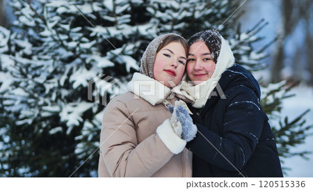 Two schoolgirls are embracing near a snowy pine tree, enjoying winter holidays together in a beautiful snowy landscape Two schoolgirls are embracing near a snowy pine tree, enjoying winter holidays together in a beautiful snowy landscape 120515336