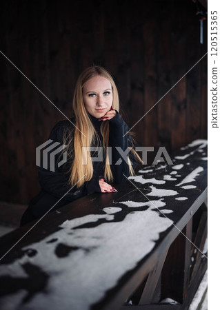 Woman with long blond hair taking a peaceful moment outdoors, resting on snowy wooden railing in winter 120515365