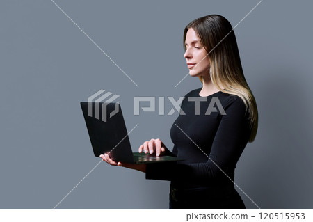 Profile view, young woman using laptop on grey studio background Profile view, young woman using laptop on grey studio background 120515953