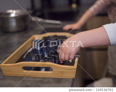 Young child joyfully uses different shaped cookie cutters in a modern kitchen, engaging in playful learning as each cookie takes form. With each new shape, cookie preparation becomes a fun experience. 120516791