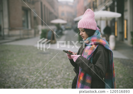 A woman in a pink hat and scarf looks at her cell phone A woman in a pink hat and scarf looks at her cell phone 120516893