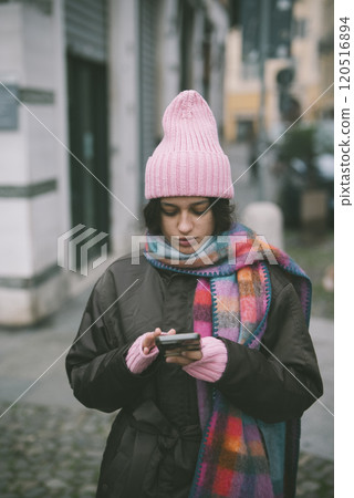 A woman in a pink hat and scarf is looking at her phone A woman in a pink hat and scarf is looking at her phone 120516894