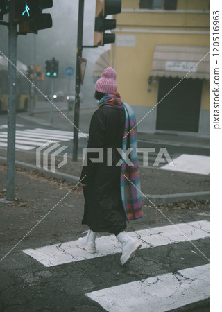 A woman who is wearing a pink hat and pink scarf is crossing the street 120516963