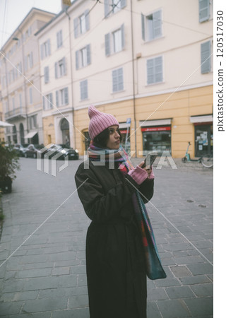A woman in a pink hat and scarf is intently looking at her phone A woman in a pink hat and scarf is intently looking at her phone 120517030