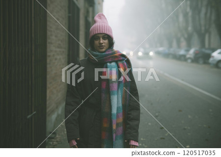 A woman in a pink hat and scarf stands on a foggy street A woman in a pink hat and scarf stands on a foggy street 120517035