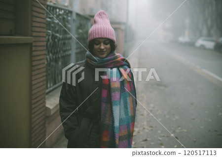 A woman in a pink hat and scarf stands on a foggy street A woman in a pink hat and scarf stands on a foggy street 120517113