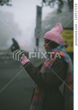 A woman in a pink hat and scarf is intently looking at her phone 120517159