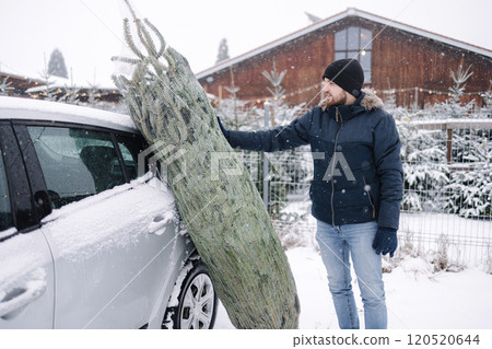 Handsome bearded man stand by the car and think how to put a Christmas tree into car Handsome bearded man stand by the car and think how to put a Christmas tree into car 120520644