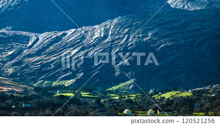 A breathtaking view features a dramatic mountain range with steep slopes and vibrant green fields nestled below. The scene is illuminated by the soft glow of morning sunlight. A breathtaking view features a dramatic mountain range with steep slopes and vibrant green fields nestled below. The scene is illuminated by the soft glow of morning sunlight. 120521256