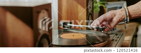 Close up of hand placing needle on vinyl record on turntable with speakers in background, detailed view highlighting turntables components and speakers 120521416