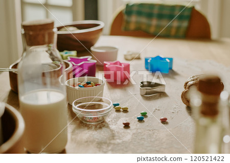 Various cookie cutters, sprinkles, and containers of milk on a kitchen table creating a lively and inviting baking scene with colorful elements and cozy atmosphere Various cookie cutters, sprinkles, and containers of milk on a kitchen table creating a lively and inviting baking scene with colorful elements and cozy atmosphere 120521422
