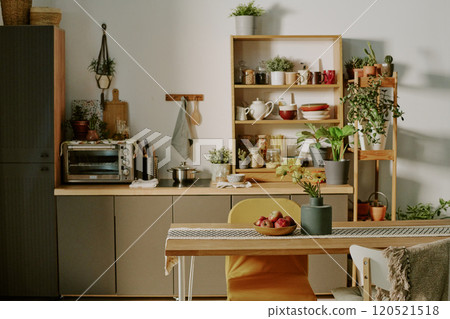 Compact and inviting kitchen setup highlighting sleek cabinets, shelving with assorted kitchenware, and variety of potted plants. Wooden table and chairs adding warmth and charm Compact and inviting kitchen setup highlighting sleek cabinets, shelving with assorted kitchenware, and variety of potted plants. Wooden table and chairs adding warmth and charm 120521518