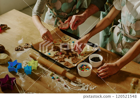 Children decorating holiday cookies in modern kitchen with various cookie cutters and colorful decorations placed on wooden table, creating festive atmosphere 120521548