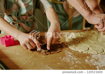 Child and adult working together on dough, cutting shapes using cookie cutter on wooden surface. Hands covered with flour and raw dough cut into various forms Child and adult working together on dough, cutting shapes using cookie cutter on wooden surface. Hands covered with flour and raw dough cut into various forms 120521609