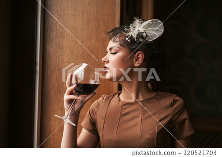Single pretty young woman with glass of red wine standing near window and looking aside at restaurant Single pretty young woman with glass of red wine standing near window and looking aside at restaurant 120521703