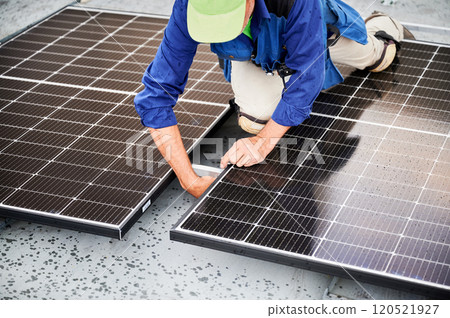 Worker building solar panel system on metal rooftop of house. Man engineer installing photovoltaic solar module outdoors. Alternative, green and renewable energy generation concept. 120521927