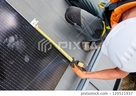 Worker building solar panel system on rooftop of house for generating electricity through photovoltaic effect. Close up man using ruler to measure mounting equipment for precise installation. Worker building solar panel system on rooftop of house for generating electricity through photovoltaic effect. Close up man using ruler to measure mounting equipment for precise installation. 120521937