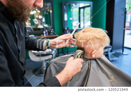 Back view of hairdresser shaving boy's head. Adorable boy getting stylish haircut. Blond kid in beauty salon. Back view of hairdresser shaving boy's head. Adorable boy getting stylish haircut. Blond kid in beauty salon. 120521949