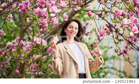 Woman allergic suffering from seasonal allergy at spring, posing in blossoming garden at springtime. Young happy woman showing holding pack of pills, giving thumbs up. Antihistamine medication concept Woman allergic suffering from seasonal allergy at spring, posing in blossoming garden at springtime. Young happy woman showing holding pack of pills, giving thumbs up. Antihistamine medication concept 120521961