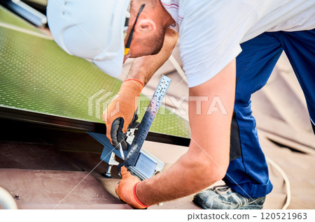 Worker building solar panel system on rooftop of house for generating electricity through photovoltaic effect. Close up man using ruler to measure mounting equipment for precise installation. Worker building solar panel system on rooftop of house for generating electricity through photovoltaic effect. Close up man using ruler to measure mounting equipment for precise installation. 120521963