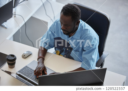 African American man working in open office environment using laptop and smartphone placed on desk while focusing on tasks with coffee cup nearby African American man working in open office environment using laptop and smartphone placed on desk while focusing on tasks with coffee cup nearby 120522337