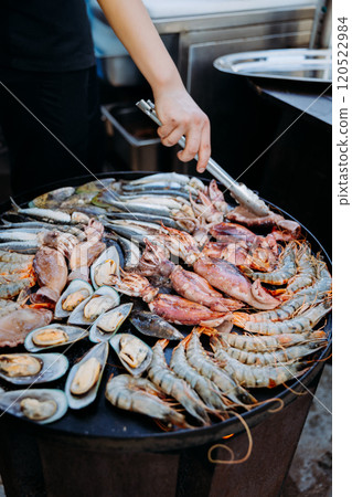 Chef grilling fresh seafood on a hot plate, showcasing shrimp, mussels, and squid for gourmet dining 120522984