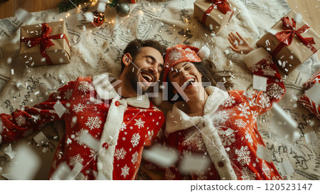 Laughing Couple On Their Backs Wearing Matching Holiday Pajamas Surrounded By Christmas Gifts. Generative AI. 120523147
