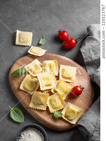 Flat lay of pasta ravioli with tomato and basil on wooden board on dark background with flour 120523767