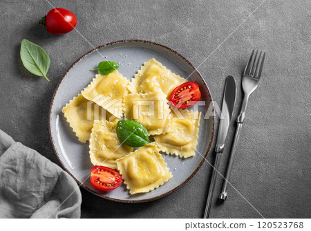 Homemade ravioli pasta with cheese, tomatoes and basil in a plate on a dark background with napkin  120523768