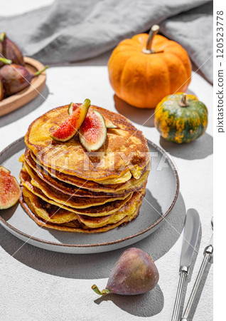 Stack of pumpkin pancakes with honey and figs on light background with fresh fruits and vegetables. Stack of pumpkin pancakes with honey and figs on light background with fresh fruits and vegetables. 120523778