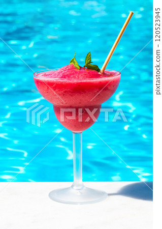 Chilled red drink on pool edge in bright sunlight. Concept of tropical refreshment and summer leisure 120523945