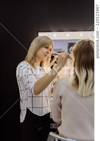 Makeup artist applying cosmetics to a client in a beauty studio with professional tools and lighting 120523987