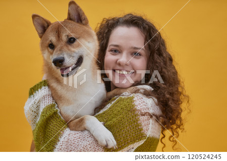 Portrait of cheerful young woman holding cute red Shiba Inu dog while posing together against yellow background in studio, copy space Portrait of cheerful young woman holding cute red Shiba Inu dog while posing together against yellow background in studio, copy space 120524245