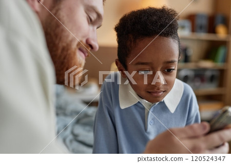 Medium shot of little Black boy looking at screen while dad showing video on phone in kids bedroom, happy adoptive family concept 120524347