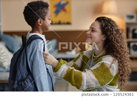 Side view of happy adoptive mother adjusting sons clothes while preparing little Black boy for school in kids room 120524361