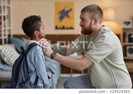 Side view of happy adoptive father adjusting sons clothes while preparing little Black boy for school in kids room 120524363